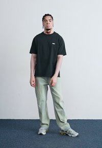 Black cotton t-shirt with a small logo, paired with light green denim pants and gray athletic shoes; solid colors with a relaxed fit.