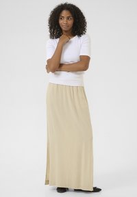 Jupe maxi beige avec fente sur le côté, en tissu doux, taille élastique ; associée à un haut ajusté à manches courtes blanc. Design simple et minimaliste.
