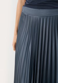 Jupe plissée en un matériau satiné bleu marine foncé. Elle présente une taille lisse et des plis verticaux qui créent du volume et de la texture.