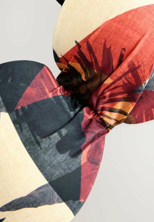 Bandeau floral en tissu multicolore avec des motifs rouges, noirs et beige, doté d'un centre noué et d'une texture lisse.