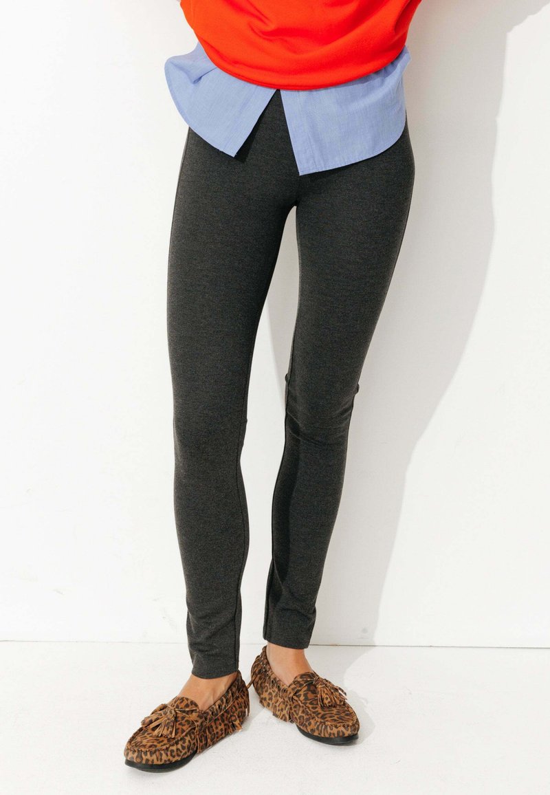 Leggings extensibles gris foncé avec une coupe ajustée et une texture lisse. Portés avec un haut orange et une chemise bleue superposée, assortis à des chaussures à imprimé léopard.