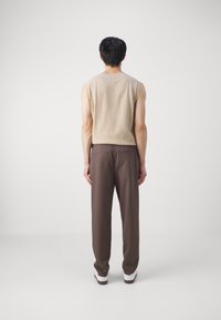 Pull sans manches beige en mélange de laine, associé à un pantalon marron. Le pantalon présente une coupe décontractée et des poches discrètes. Des chaussures neutres complètent le look.