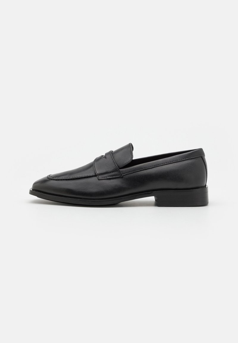 Chaussure loafer homme en cuir noir avec un petit talon et un design classique à bride penny, vue de profil sur un fond blanc uni.