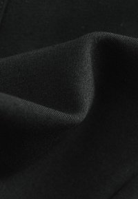 Schwarzer Stoff mit glatter Textur, der eine gefaltete Kante und ein feines Strickmuster zeigt, das Flexibilität und Weichheit illustriert.