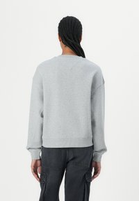 Felpa grigia con spalle scese, polsini a costine e orlo a costine. Texture morbida e design minimalista, indossata con pantaloni cargo scuri.