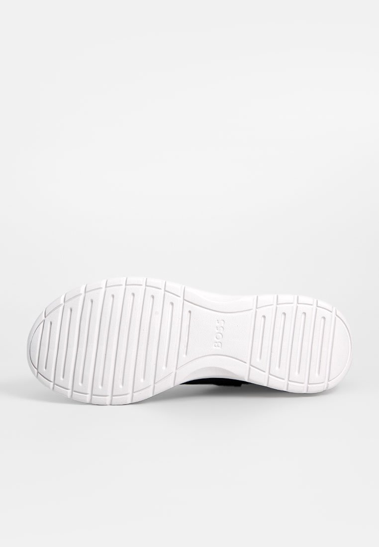 Podeszwa buta w białej gumie z teksturowanym wzorem antypoślizgowym; posiada zaokrąglony obcas i wytłoczone logo po boku.