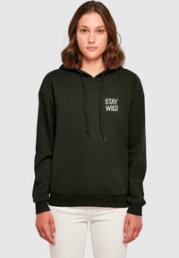 Felpa nera con cappuccio e cordini, caratterizzata da una grafica bianca "STAY WILD" sul lato sinistro del petto. Texture morbida, vestibilità rilassata e polsini a costine.