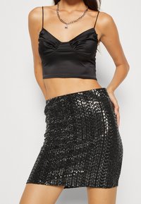 Černý saténový crop top s plisovaným detailem a tenkými ramínky, doplněný těsnou černou mini sukní s flitry a lesklou texturou.