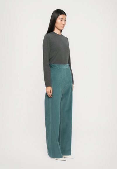 Gray long-sleeve shirt paired with high-waisted, wide-leg teal corduroy pants. Model stands sideways, showcasing the fabric texture and cut.