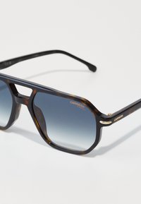 Occhiali da sole tartarugati con design geometrico, lenti grigie sfumate, dettagli dorati e una sofisticata intaglio nel ponte per un ulteriore interesse visivo.