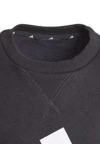 Sudadera negra con cuello y puños de canalé. Presenta detalles de costura visibles y cinta de marca en el interior del cuello. Textura suave.