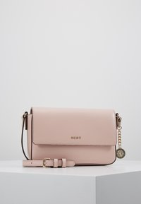 Růžová kožená crossbody kabelka s klopou, zlatými detaily a odnímatelným charmem. Má texturovaný povrch a nastavitelný popruh.