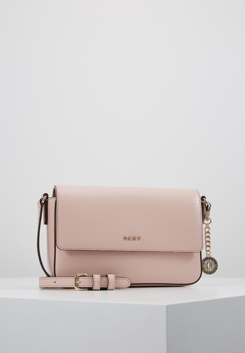 Růžová kožená crossbody kabelka s klopou, zlatými detaily a odnímatelným charmem. Má texturovaný povrch a nastavitelný popruh.