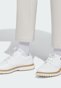 Λευκά παπούτσια γκολφ με επάνω μέρος από δέρμα, λαστιχένια σόλα και αντίθετη ραφή. Σχεδιασμένα με στρογγυλή μύτη και μοναδικό σύστημα κλεισίματος χωρίς κορδόνια.