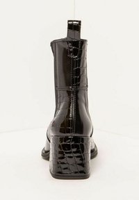 Botín al tobillo de charol negro con textura de cocodrilo, tacón cuadrado y una lengüeta en la parte trasera. Acabado suave sin patrones visibles.