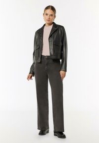 Schwarze Lederjacke mit verkürztem Schnitt, zwei Fronttaschen, kombiniert mit hochgeschnittenen, dunkelgrauen Jeans und schwarzen Stiefeln. Darunter ein hellrosa Oberteil.