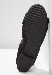Chaussure marine avec une semelle en caoutchouc noir flexible présentant des arêtes marquées. Tige en tissu sans motifs ni détails matériels discernables.