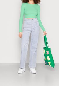 Ljusgrön, långärmad crop top i kombination med ljusblå vida jeans och vita plattformssneakers. Håller en grön tote med färgglada blommönster.