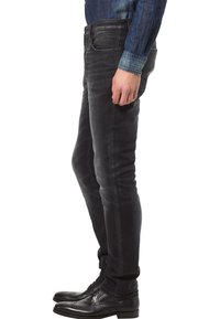 Czarne jeansy o wąskim kroju wykonane z denimu o gładkiej fakturze. Posiadają pięć kieszeni i klasyczny pas, zestawione z czarnymi skórzanymi butami.