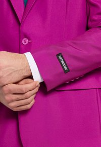 Magenta maßgeschneiderte Sakko mit einem einreihigen Knopfverschluss, ausgestattet mit einem weißen Hemdaufschlag und einem schwarzen Etikett mit der Aufschrift "SUITMEISTER."