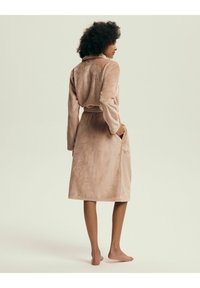 Soft, beige plush bathrobe with long sleeves, a belted waist, and side pockets, featuring a relaxed fit and smooth texture.