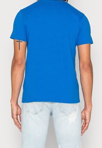 Modrá bavlněná tričko s kulatým výstřihem a krátkými rukávy. Má hladkou strukturu a klasický střih, nošené s světle modrými ošoupanými džíny.
