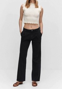 Top corto blanco con textura acanalada y bordes en forma de ondas, combinado con pantalones de pierna ancha negros y sandalias de tiras marrones.