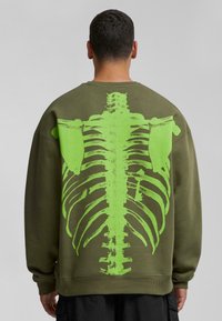 Olijfgroene sweatshirt van katoen, met een grote, felgroene ribbenkastafdruk op de achterkant. Standaard pasvorm, ribgebreide manchetten.