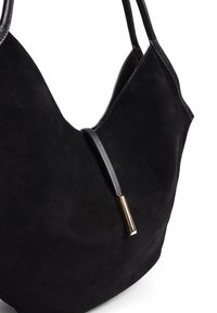 Melna zamša soma ar mīkstu tekstūru, V formas dizainu, divām melnām siksnām un dekoratīvu zelta akcentu uz melna ādas detaļas.