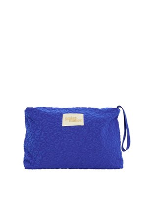 Pochette en tissu bleu texturé avec une lanière pour le poignet et une étiquette beige indiquant "grain de malice" au centre avant.