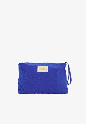 Pochette en tissu bleu texturé avec une lanière pour le poignet et une étiquette beige indiquant "grain de malice" au centre avant.