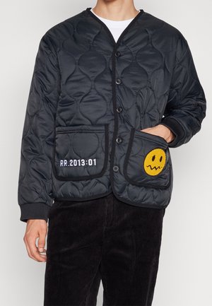 Svart quiltad jacka med knapplås, ficka med gul smileygrafik, texturerat tyg, detaljerad med vit broderi.