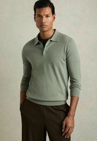 Polo shirt tricotat de culoare verde deschis, cu guler, închidere cu trei nasturi și manșete ribbate, asortat cu pantaloni texturați de culoare maro.