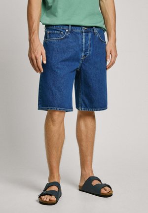 Shorts in denim blu scuro con una vestibilità rilassata, dotati di cinque tasche, passanti per la cintura e cuciture in evidenza. Abbinati a sandali scuri.