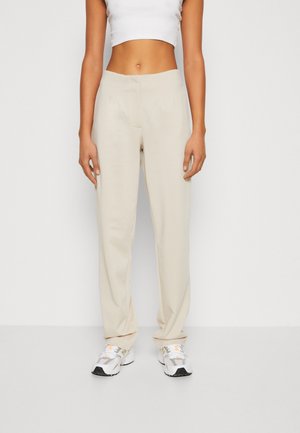 Beige, lette bukser med lige pasform, der har forreste læg og sidelommer, parret med hvide og multifarvede sportssko.