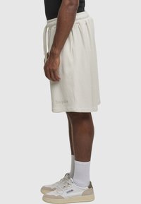 Kremfarvede ribstrikkede shorts med elastisk taljebånd og snøre. Broderet logo på benet. Båret med hvide sneakers og sokker.