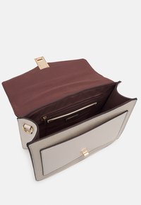 Beige handväska med en texturerad yta, brun tyginteriör och ett guldspänne. Innehåller en dragkedjeficka och gott om plats för förvaring.