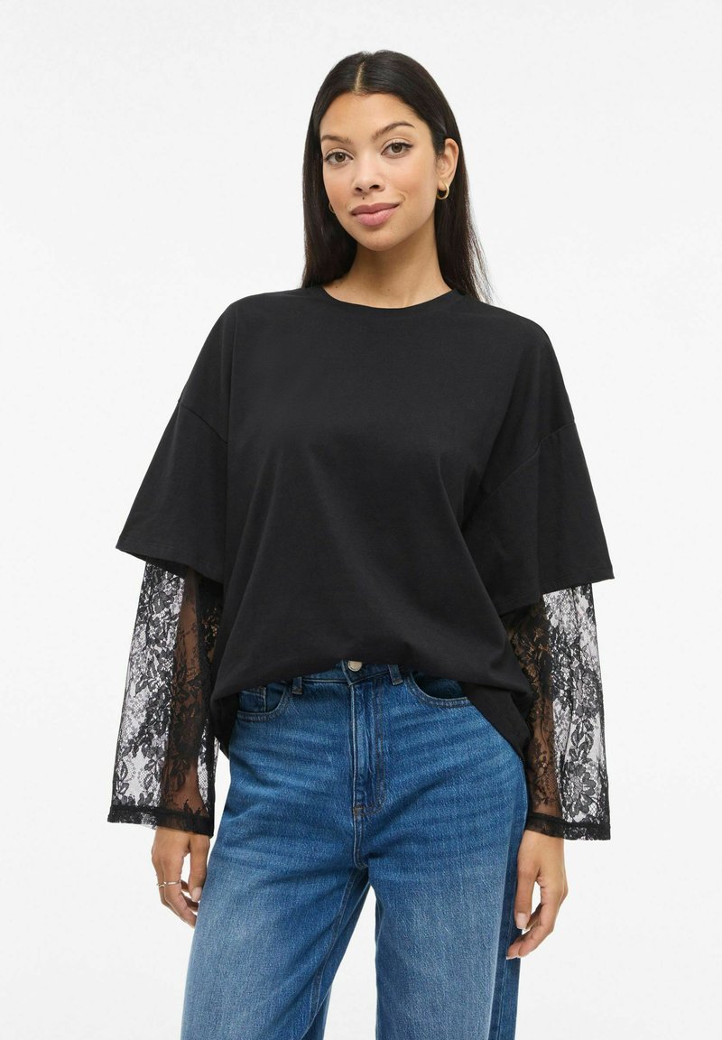 Svart oversized t-skjorte med lange ermer i blonde. Mykt bomullsmateriale, rund halslinning og avslappet passform kombinert med blå denimjeans.