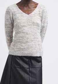 Jasnoszary sweter w serek z teksturowanej, puszystej tkaniny. W połączeniu z czarną skórzaną spódnicą z poziomymi szwami i gładkim wykończeniem.