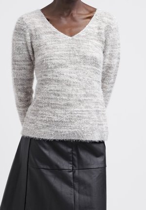 Maglione grigio chiaro a V con tessuto texture e peloso. Abbinato a una gonna in pelle nera con cuciture orizzontali e una finitura liscia.