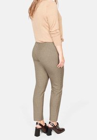 Pantaloni marroni a quadri con un design aderente, abbinati a una maglietta beige e scarpe con tacco marroni. Il tessuto presenta una leggera texture.