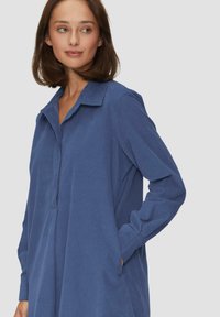 Langärmliges, blaues Shirtkleid aus strukturiertem Stoff mit Kragen und halbknöpfbarer Leiste. Verfügt über Seitentaschen.