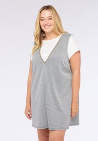 Grau-weißer Hahnentrittkleid mit V-Ausschnitt, das aus einem strukturierten Stoff besteht und einen goldenen Besatz entlang des Ausschnitts hat, mit kurzen Ärmeln.