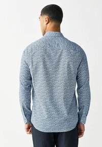 Garums piedurknes krekls ar zilu ziedu rakstu uz viegla auduma. Klasiska apkakle, pogu aproces un izliekts apakšmalas dizains.