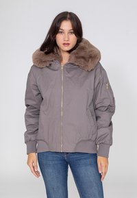 Graue Bomberjacke mit einem großen, flauschigen braunen Pelzkragen. Verfügt über einen Frontreißverschluss und elastische Bündchen an den Ärmeln und am Saum.