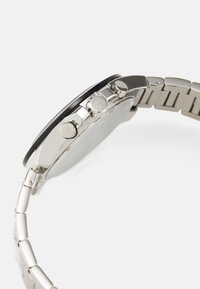 Reloj de acero inoxidable plateado con una esfera redonda, tres botones en el lado derecho y una correa de pulsera lisa y pulida.