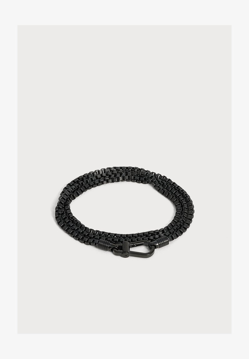 Chaîne métallique tissée noire avec un fermoir mousqueton noir, enroulée sur un fond gris clair.