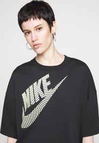 Musthave suurustega must T-särk, mille esiküljel on suur, punktidega kollane Nike logo. T-särk on klassikalise ümarate kaelustega ja lühikeste varrukatega.