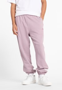 Lavendelfarbene Jogginghosen mit elastischen Bündchen und Bund, ausgestattet mit Seitentaschen und einem kleinen Logodetail. Kombiniert mit weißen Sneakers.