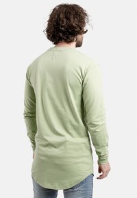 Lange mouwen shirt in lichtgroen, met een ronde halslijn, gebogen onderrand, en zachte katoen, gedragen met blauwe jeans.
